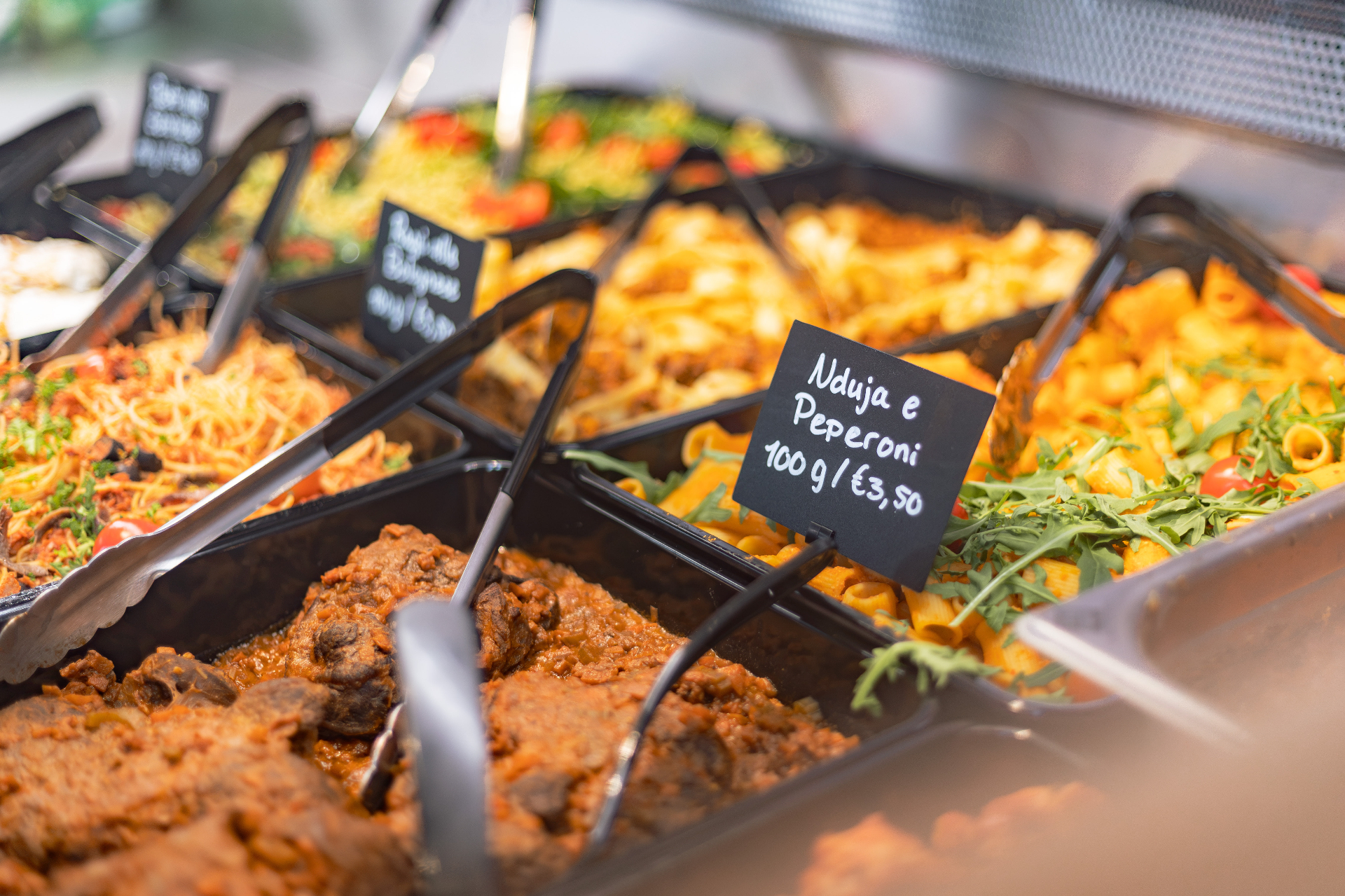 Vers bereide pasta's en gerechten in de vitrine van Mercato Tomato